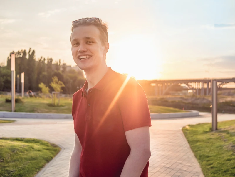 Junger Mann steht draußen lächelend, sonne hinter ihm