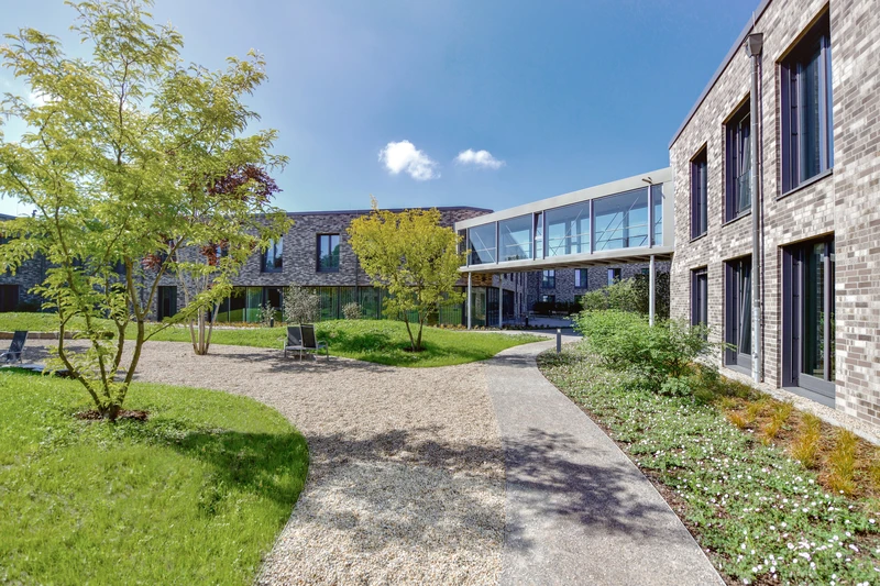 Innenhof der Oberberg Fachklinik D&uuml;sseldorf-Kaarst mit modernen Backsteingeb&auml;uden, begr&uuml;nten Wegen und verglastem Verbindungsgang