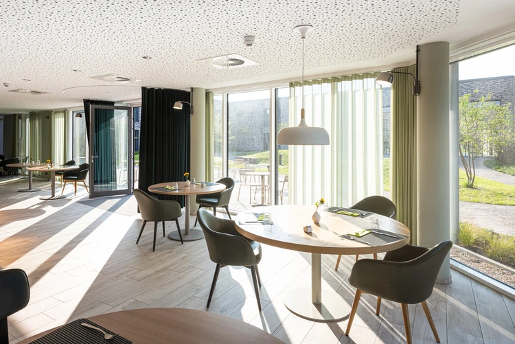 Heller Speisesaal mit runden Tischen und Blick in den Innenhof