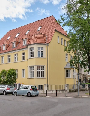Gelbes mehrst&ouml;ckiges Eckgeb&auml;ude in einer Wohnstra&szlig;e mit Parkpl&auml;tzen und B&auml;umen &ndash; Au&szlig;enaufnahme der Oberberg Tagesklinik Hannover