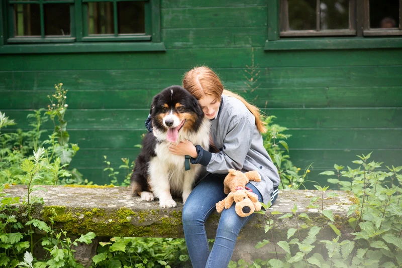Frau sitzt mit einem Hund drau&szlig;en l&auml;chelnd