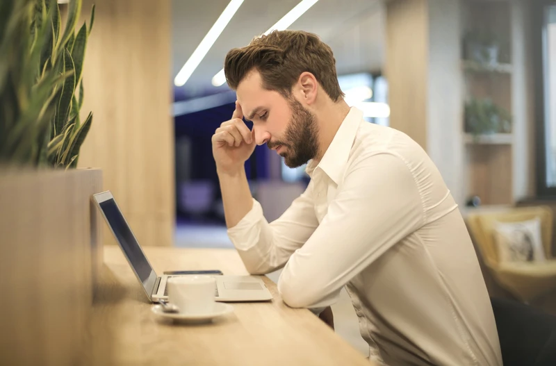 Mann sitzt mit Kopfschmerzen vor dem Laptop