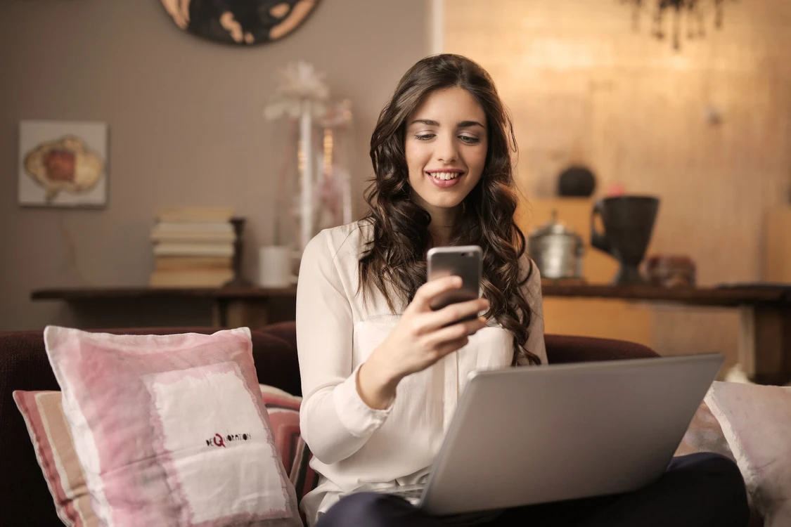 Frau sitzt vor ihrem laptop und schaut ihr handy
