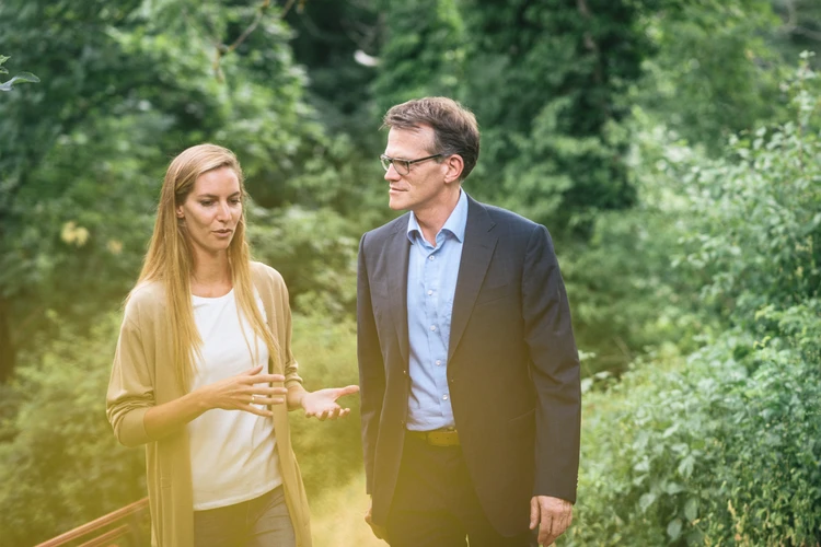 Therapeut und Patientin gehen im Garten und unterhalten sich.
