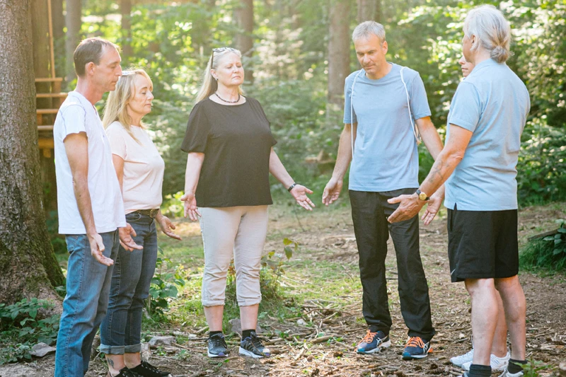 Eine therapiegruppe steht draußen in der natur im kreis mit offenen händen